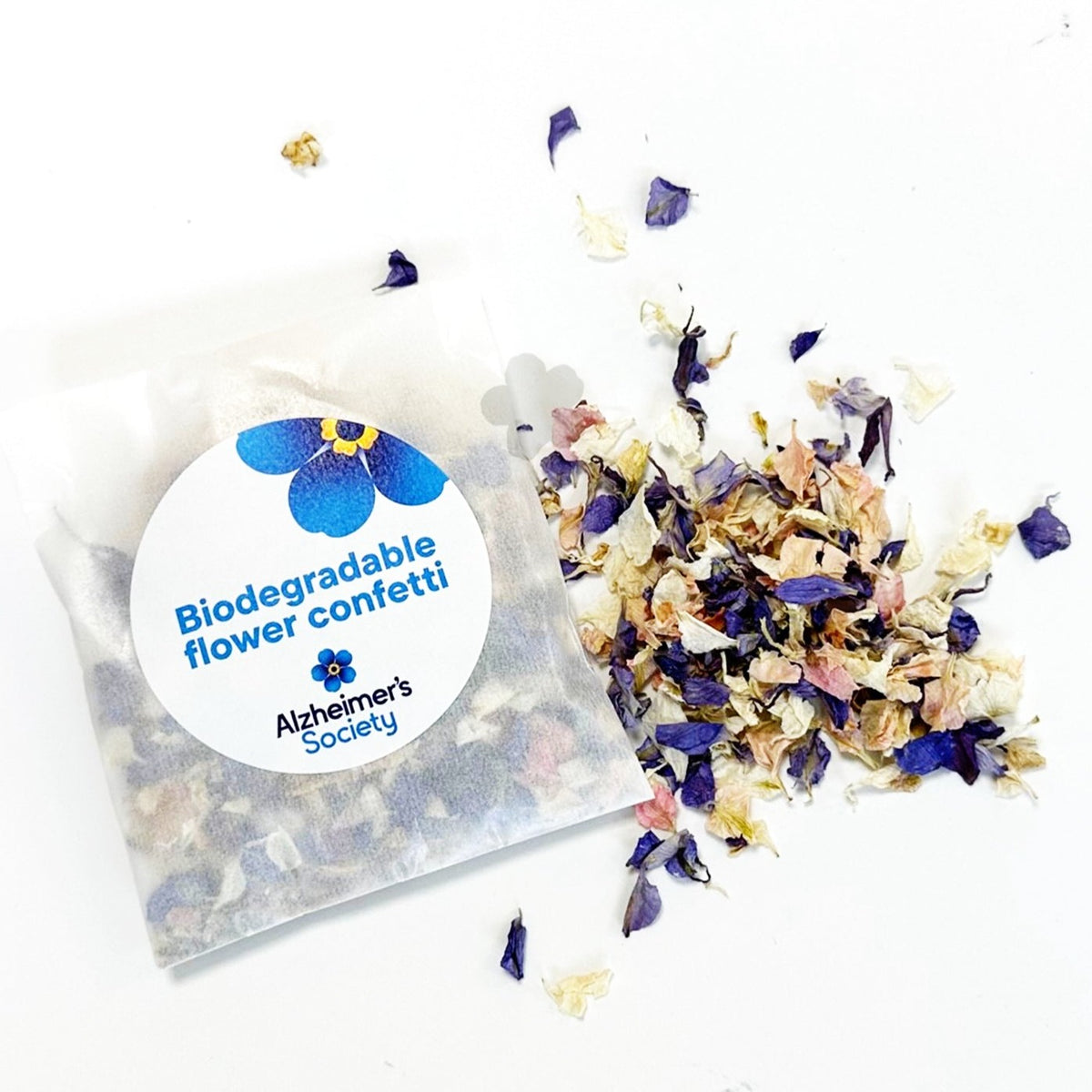 A paper bag which shows the contents of white, pink, blue dried delphinium flower confetti. A sticker on the bag says biodegradable flower confetti and has the Alzheimer&#39;s Society logo too.