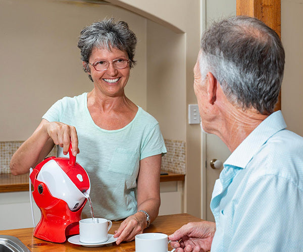 a smiling older woman easily pouring a cup of tea using an assistive kettle