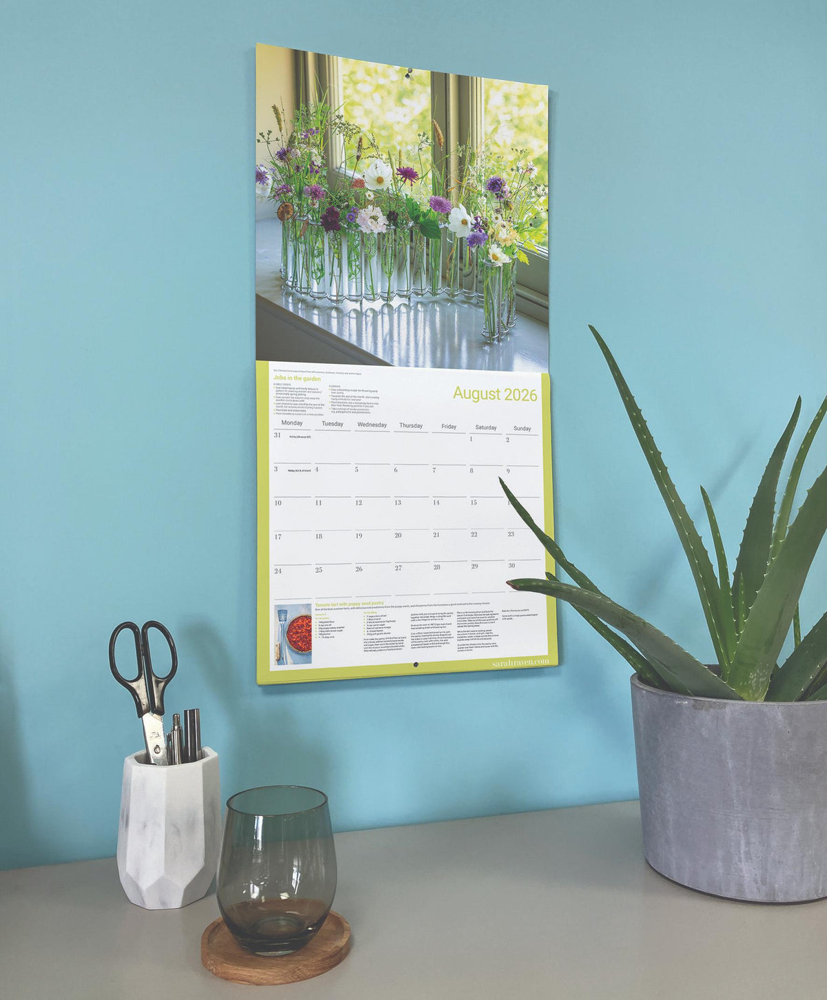 Calendar on a wall with a plant and desk items below