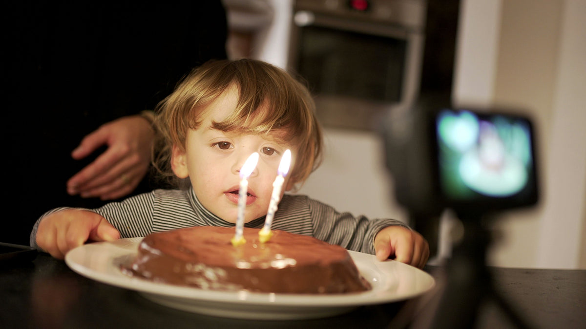 Child blowing out candles on a birthday cake with a camera recording the moment.