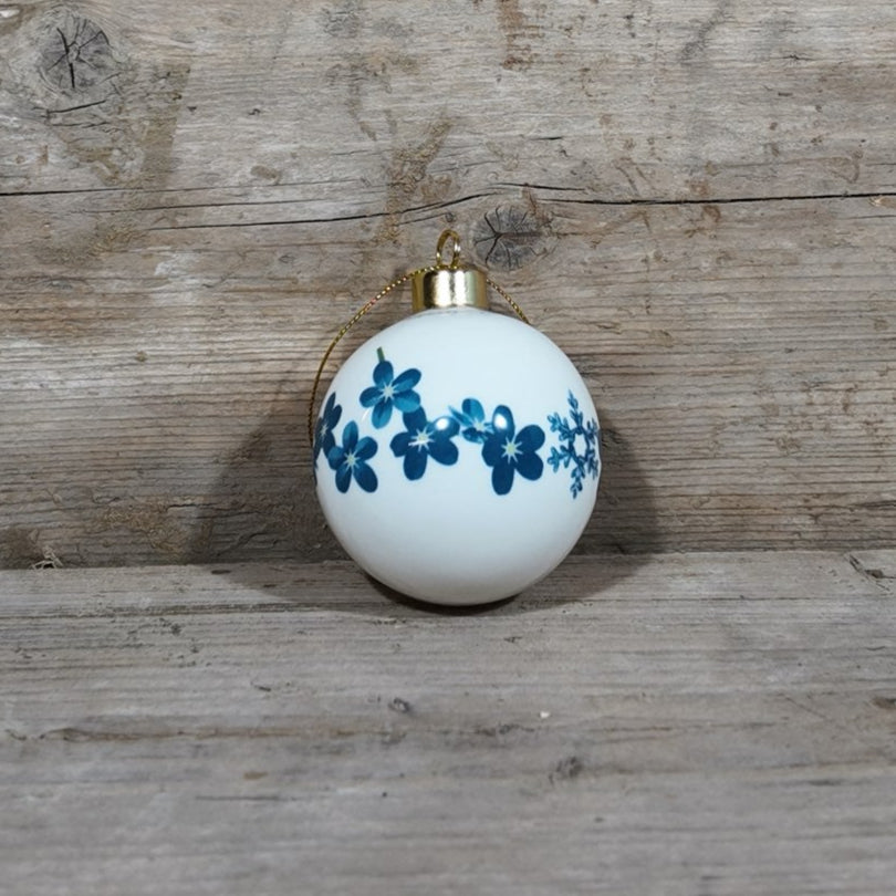 White ornament with blue forget-me-not and snowflake pattern on a wooden surface