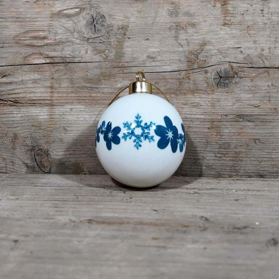 White ornament with blue forget-me-not and snowflake design on a wooden surface