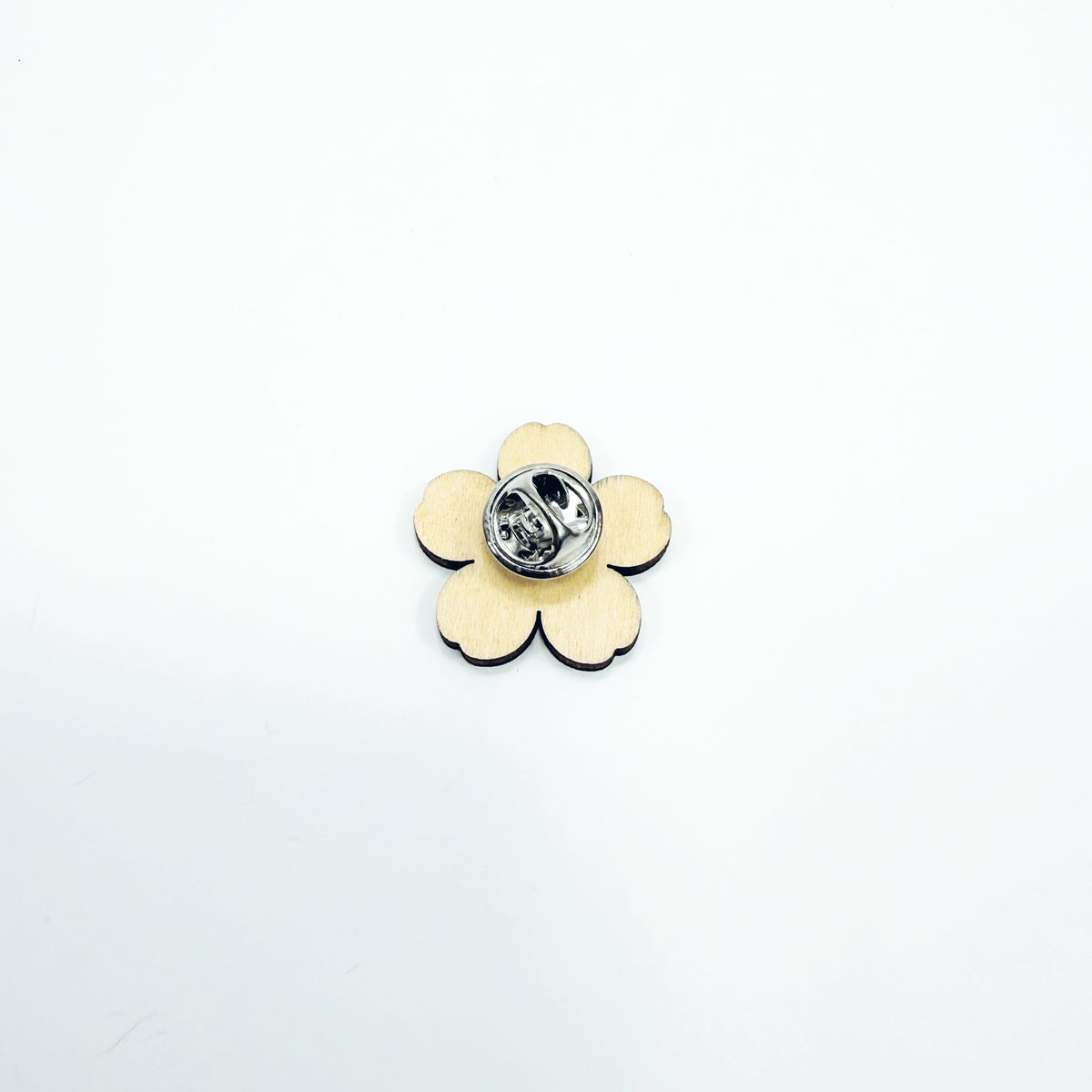 The back of a wooden forget-me-not pin badge showing the silver clasp