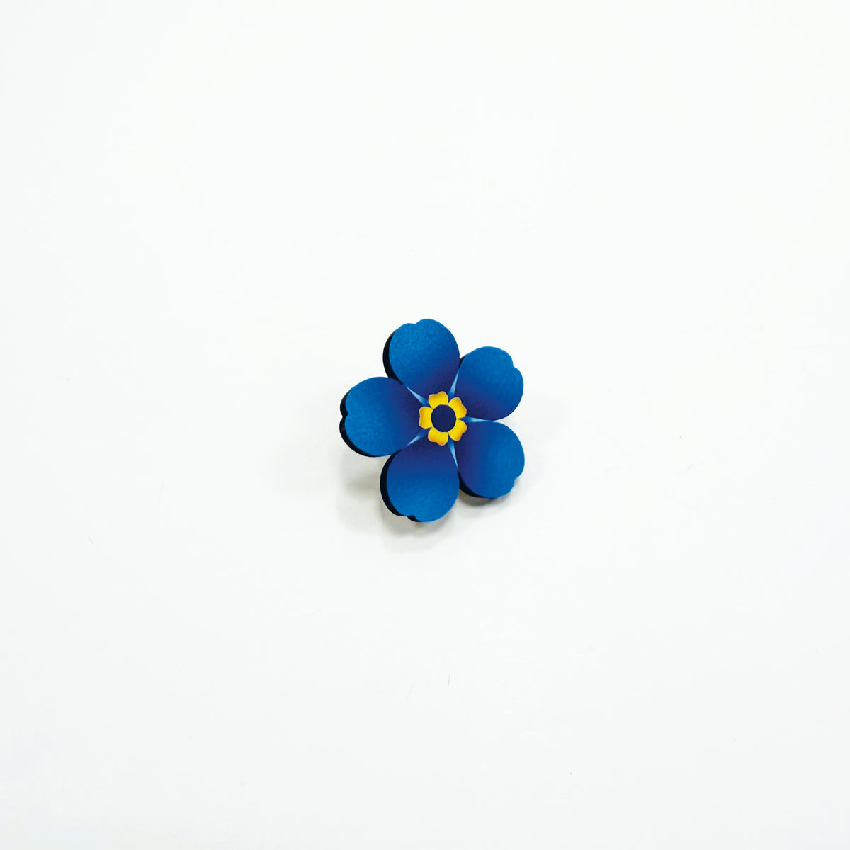 A blue wooden forget-me-not pin badge on a white background