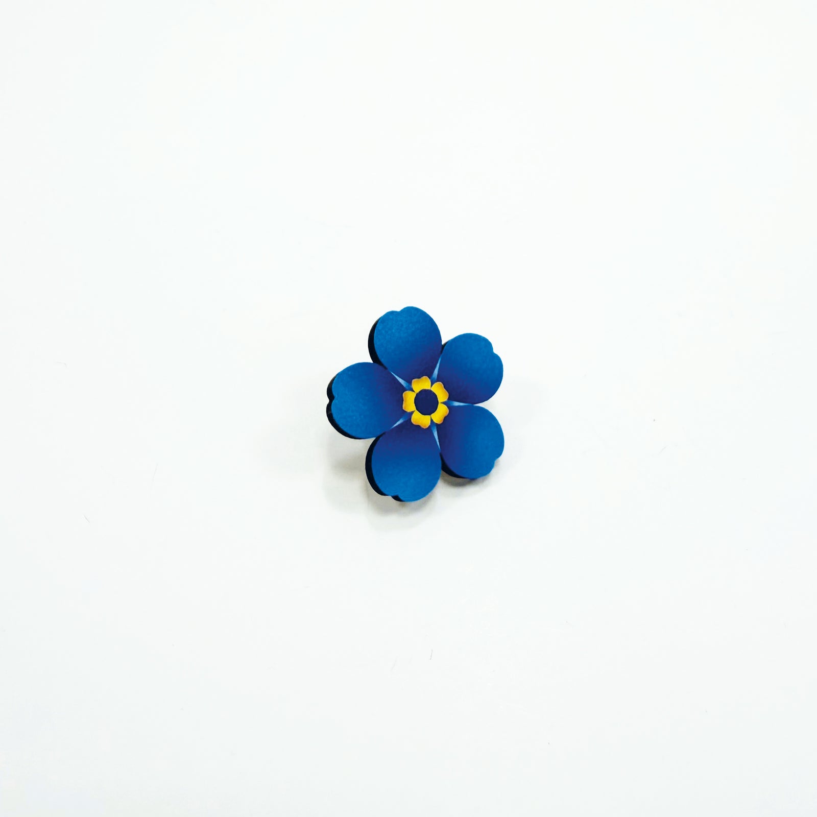 A small wooden forget-me-not pin badge on a white background