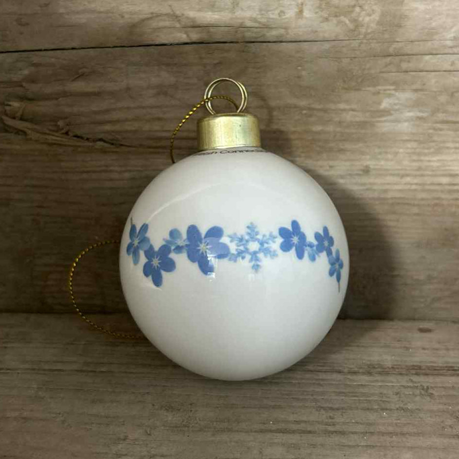 White Christmas ornament with blue forget-me-not and snowflake pattern on a wooden surface