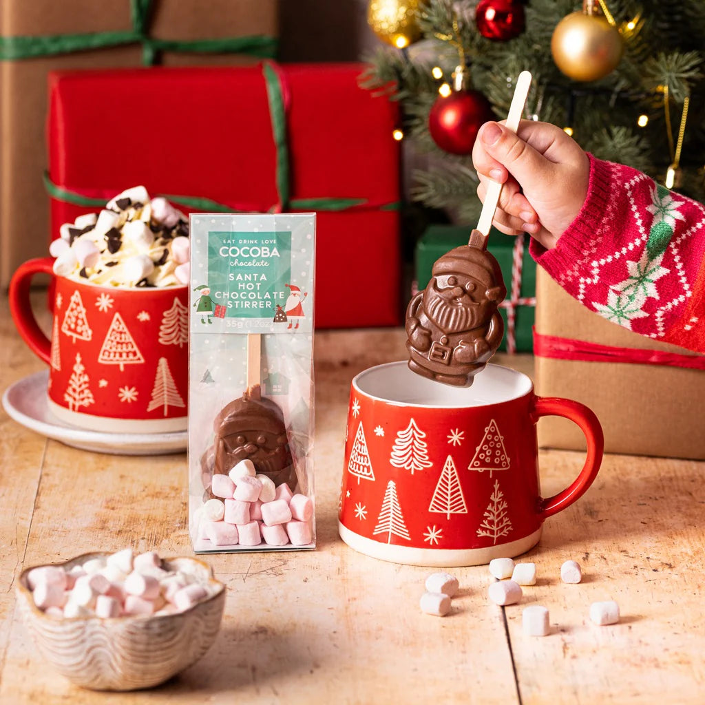 Santa hot chocolate stirrer being dipped in a festive mug. 