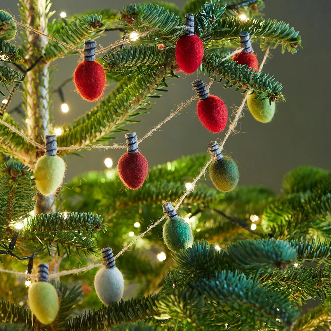 Decorative felted string lights with red, green, and white bulbs on a Christmas tree.