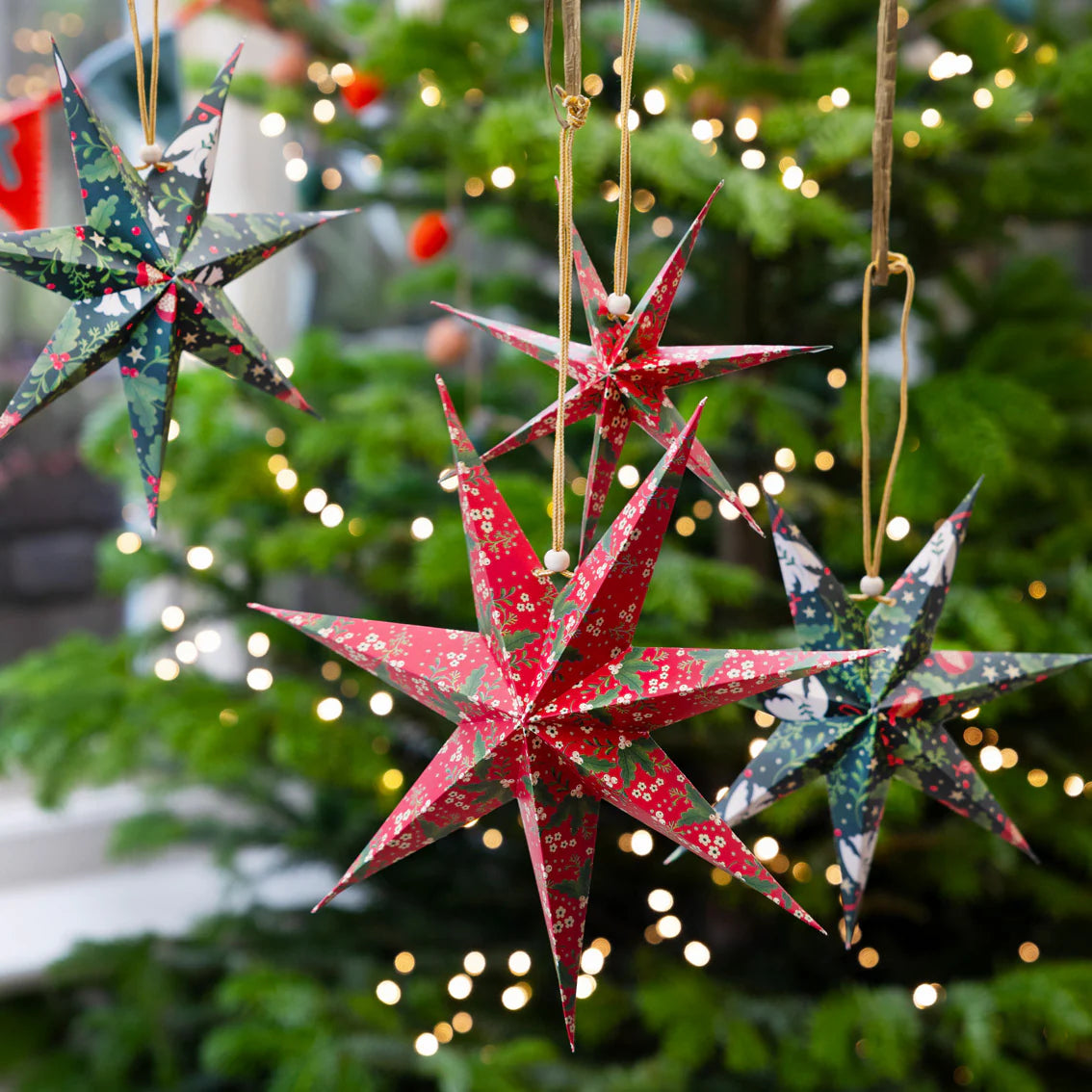 Decorative paper stars hanging against a Christmas tree with lights.