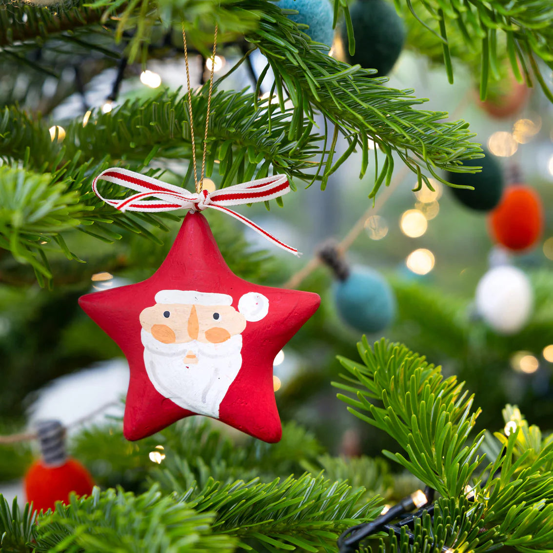 Red star-shaped Christmas ornament with Santa Claus face on a green tree