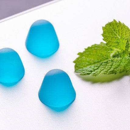 Three minty blue gummy sweets on a white background with a mint leaf.
