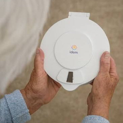 White idem pill dispenser held by hands - a small window is visible in the dispenser.