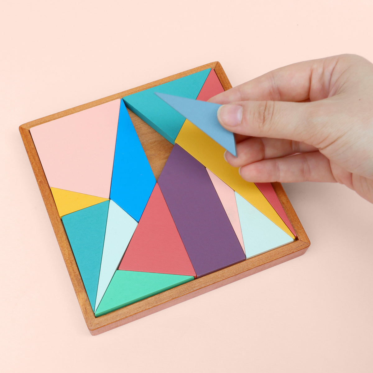 A hand placing a shape into a tray to form a coloured square out of different shapes.