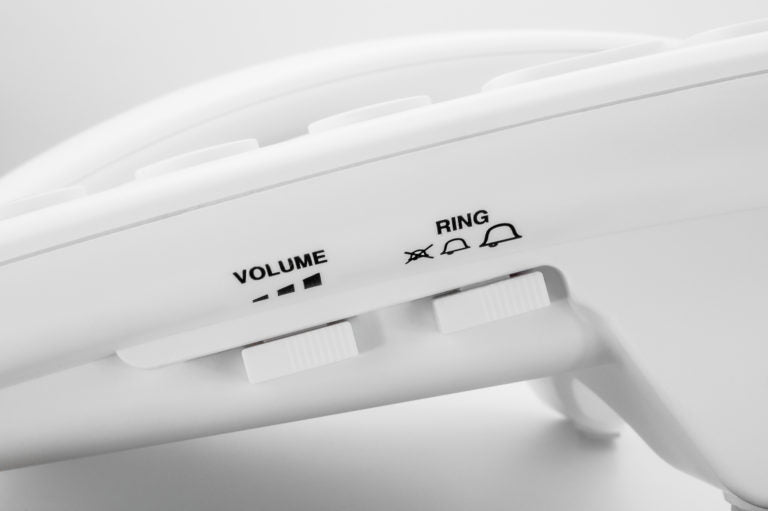 Close-up of a white electronic landline phone showing the side controls with labels 'VOLUME' and 'RING' and corresponding switches.