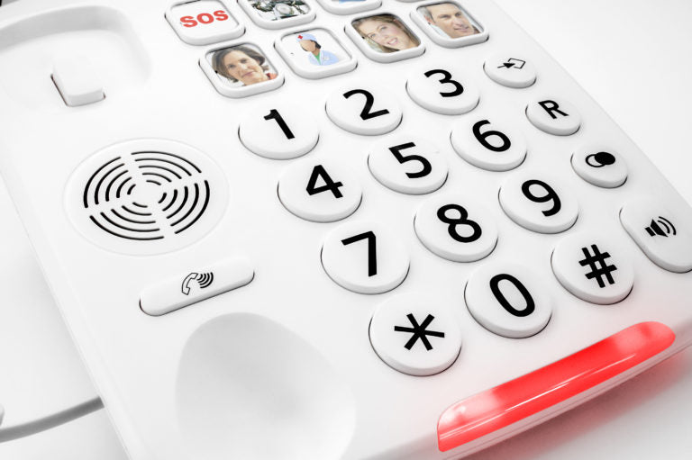 A close-up of a white landline telephone keypad with a red flashing button along the bottom edge, showing number buttons and small call name icons.