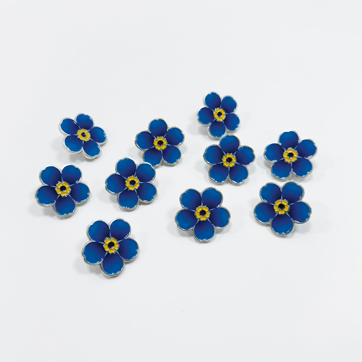 10 blue metal forget-me-not pin badges on a white background