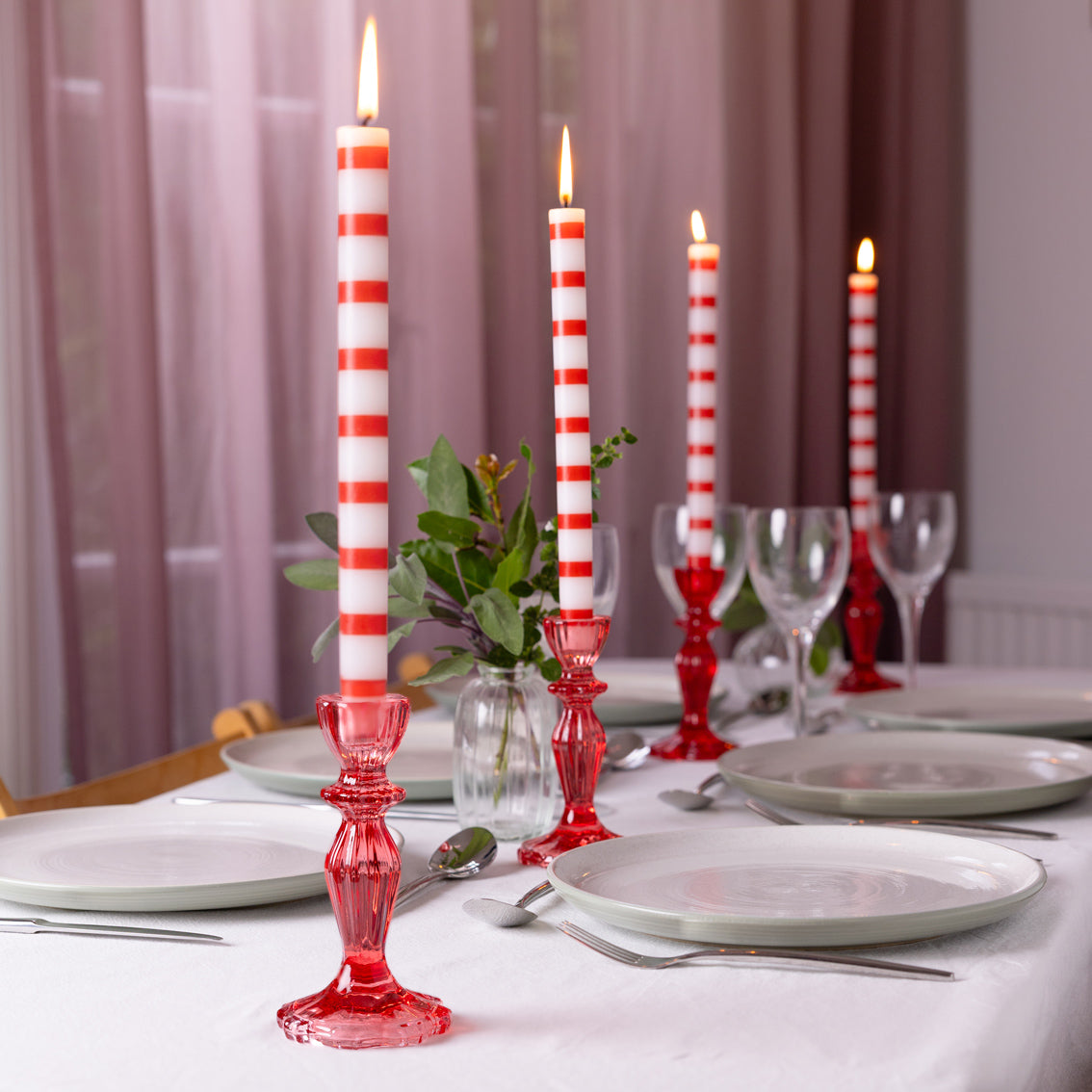 Dining table setting with red and white striped candles in decorative holders.