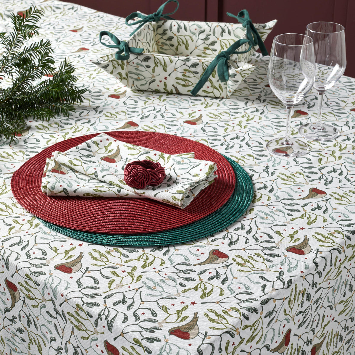Robin and mistletoe tablecloth with placemats and napkins on top and wine glasses in the background.