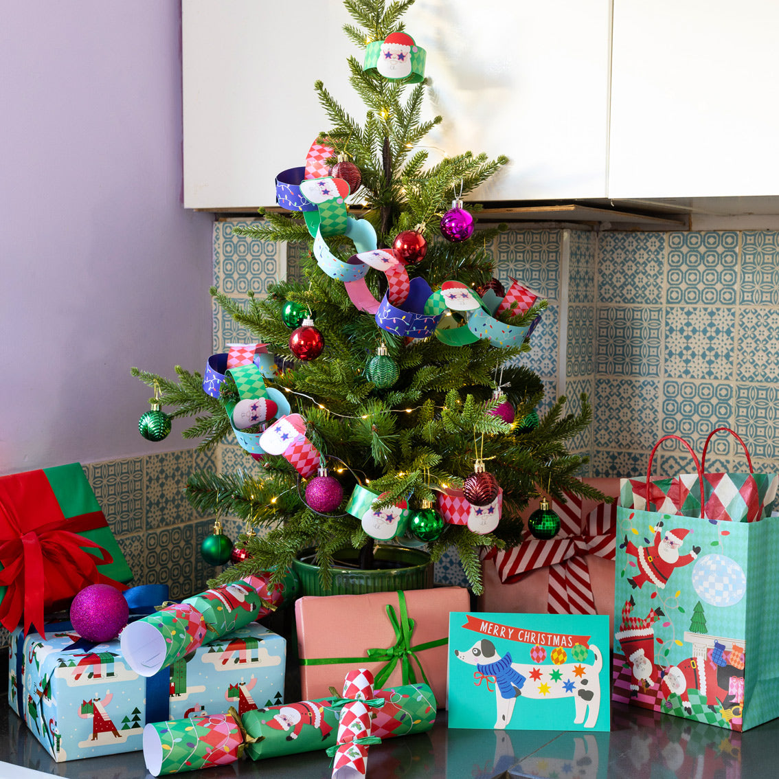 Decorated Christmas tree featuring Santa paper chains with ornaments and presents in a kitchen setting
