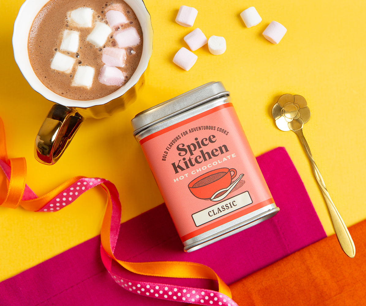 Spice Kitchen tea canister with a cup of hot chocolate and marshmallows on a colorful background