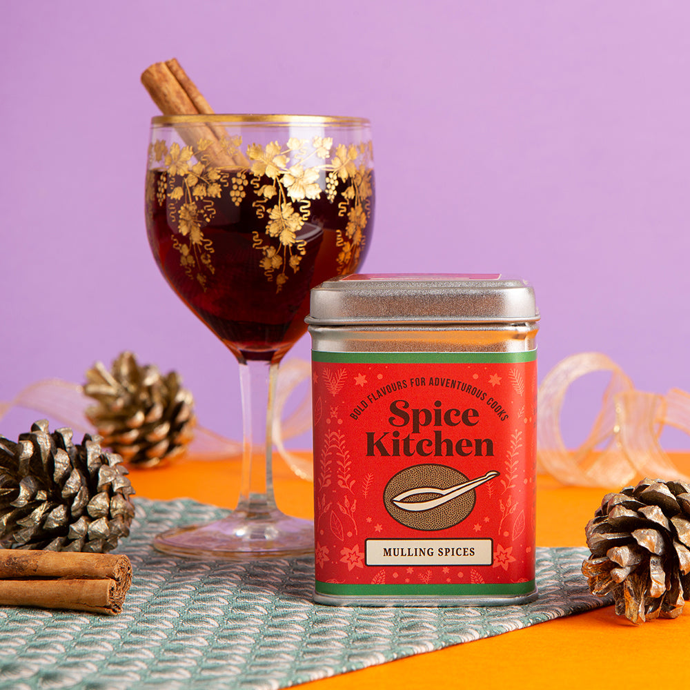 Spice Kitchen millling spices can with a glass of mulled wine and pine cones on a colorful background