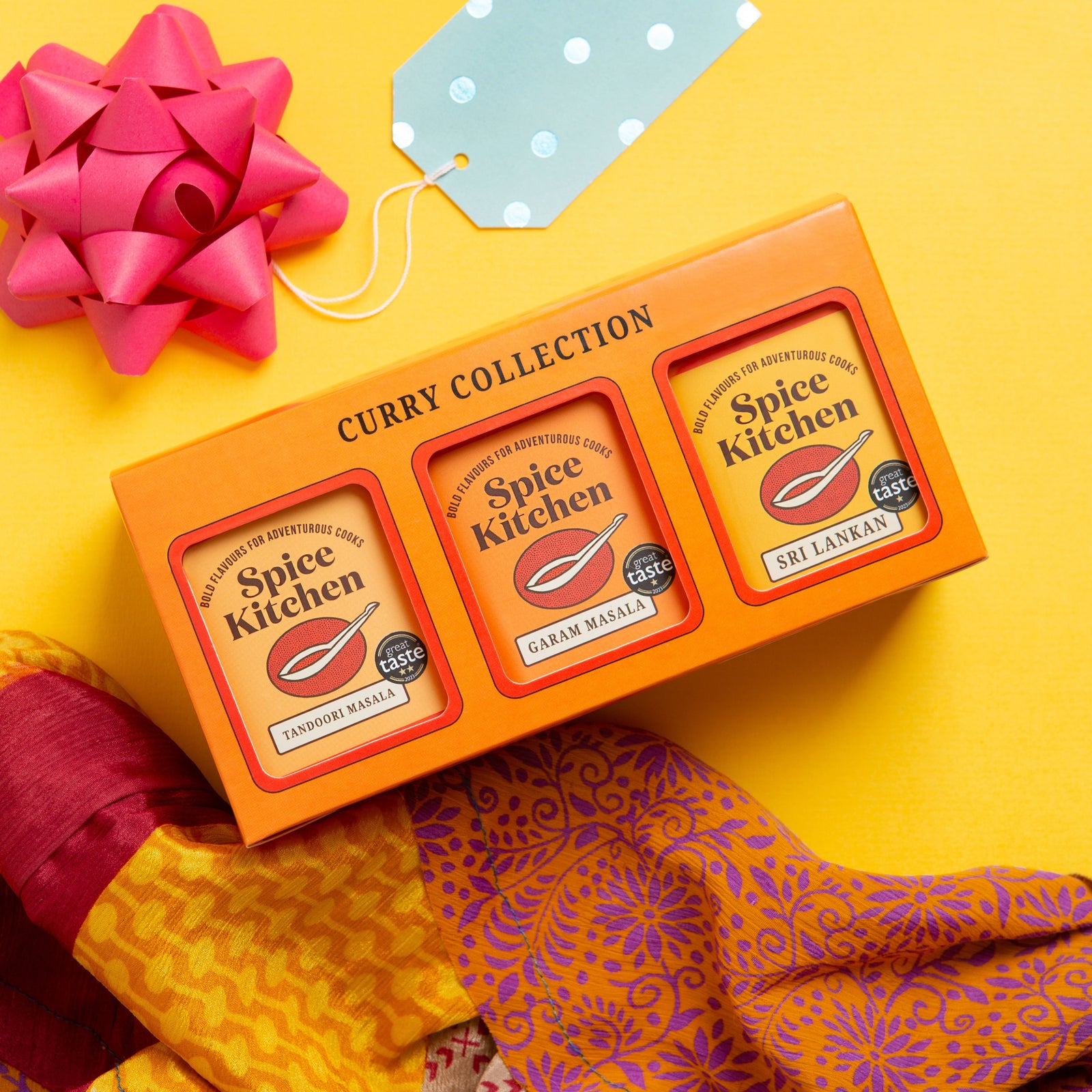 Spice Kitchen Curry Collection packaging with a pink bow on a yellow background