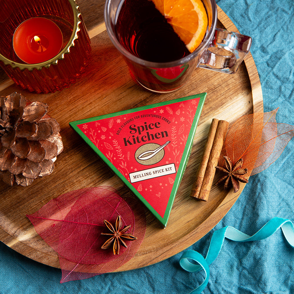 Spice kit with a glass of tea and cinnamon sticks on a wooden tray against a blue fabric background