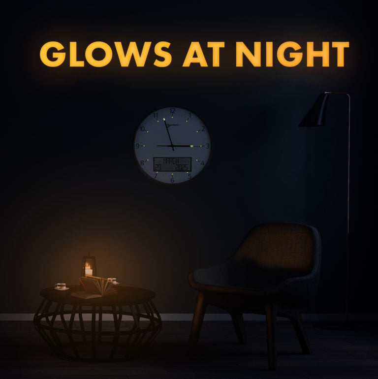 Large white analogue clock with digital display on a wall in the dark with GLOWS AT NIGHT text, to display night-time visibility. 