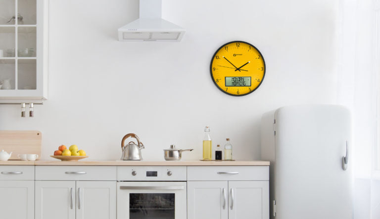 Large yellow analogue clock with digital display on a wall in a kitchen.