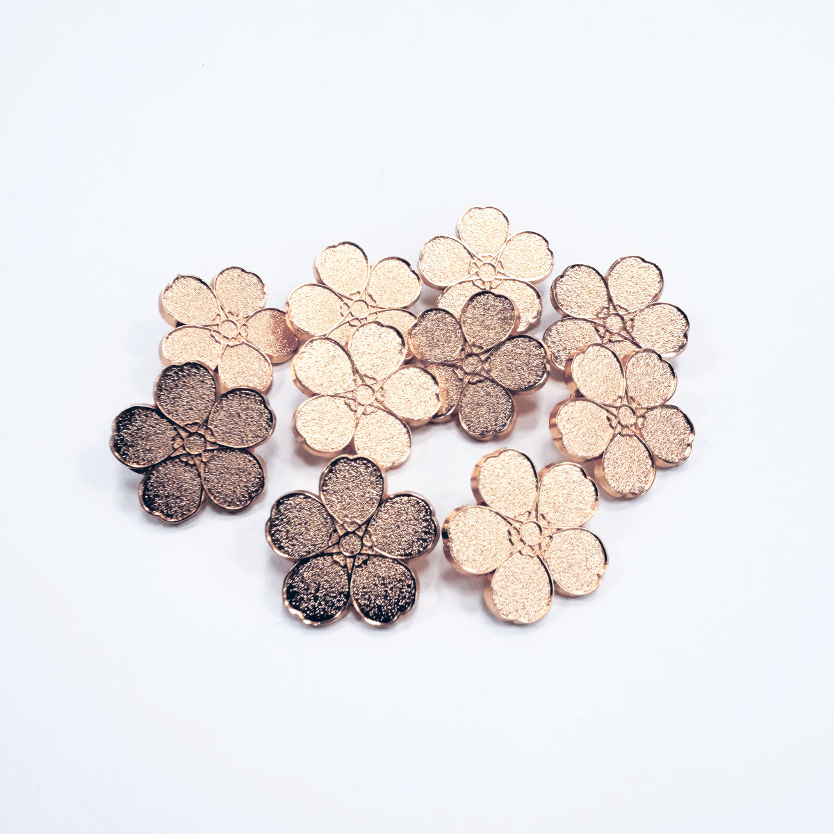 10 Rose gold metal forget-me-not pin badges on a white background