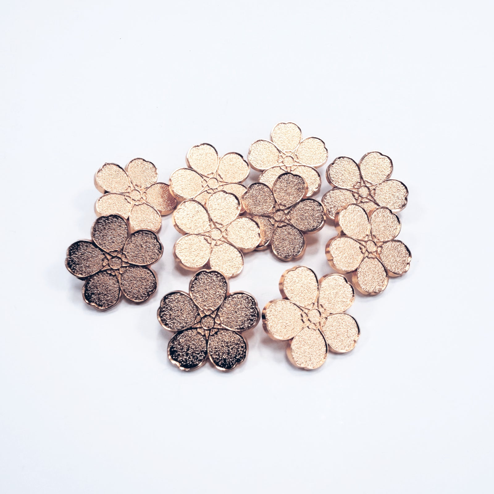10 Rose gold metal forget-me-not pin badges on a white background