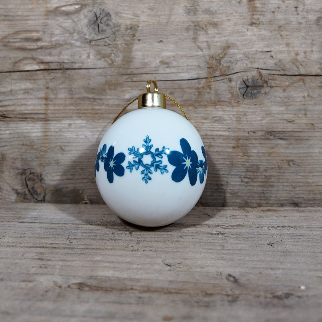 White ornament with blue forget-me-not and snowflake pattern on a wooden surface