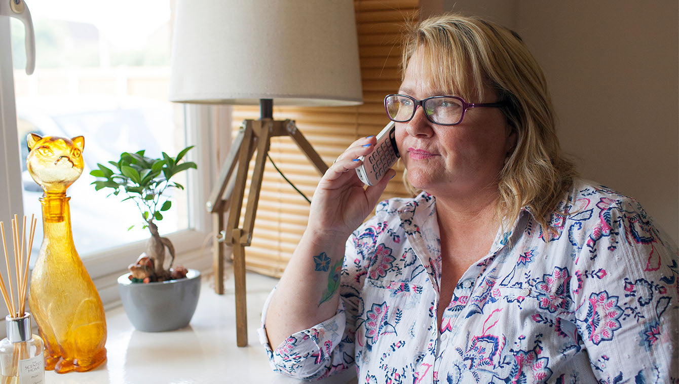 Woman talking on a phone in a home setting with decor elements.