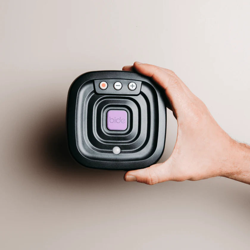 Hand holding a black device with 'bide' branding on a beige background