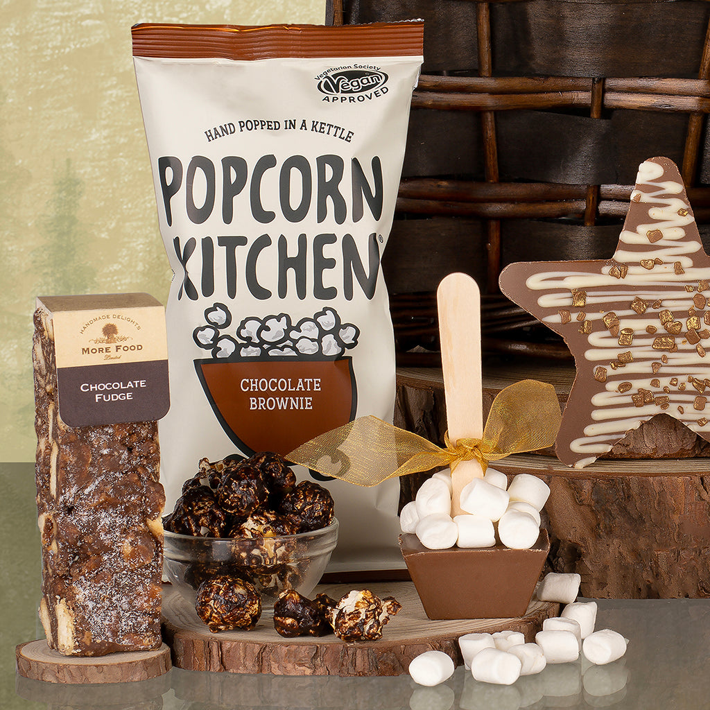 Chocolate brownie popcorn bag with a chocolate fudge bar, marshmallow stirrer and star shaped chocolate in the background.