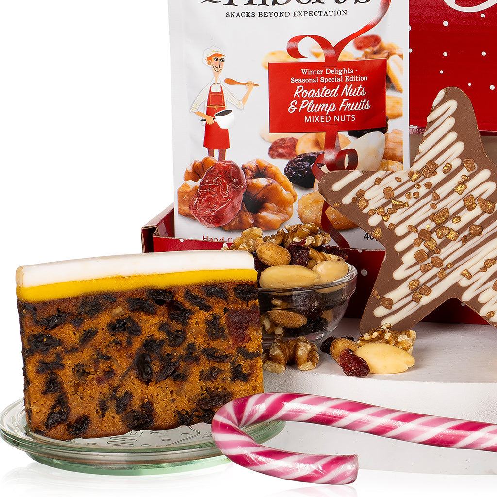 Christmas fruit cake with a star-shaped decoration, candy cane, and mixed nuts packaging on a white background.