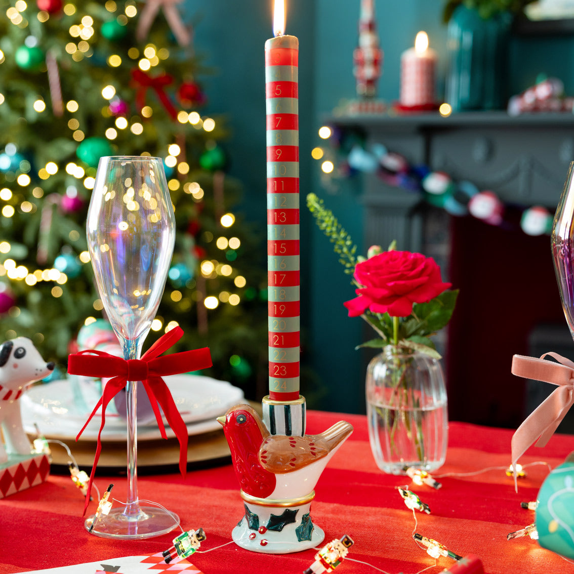Decorative Christmas table setting with advent candle, glasses, and a rose.