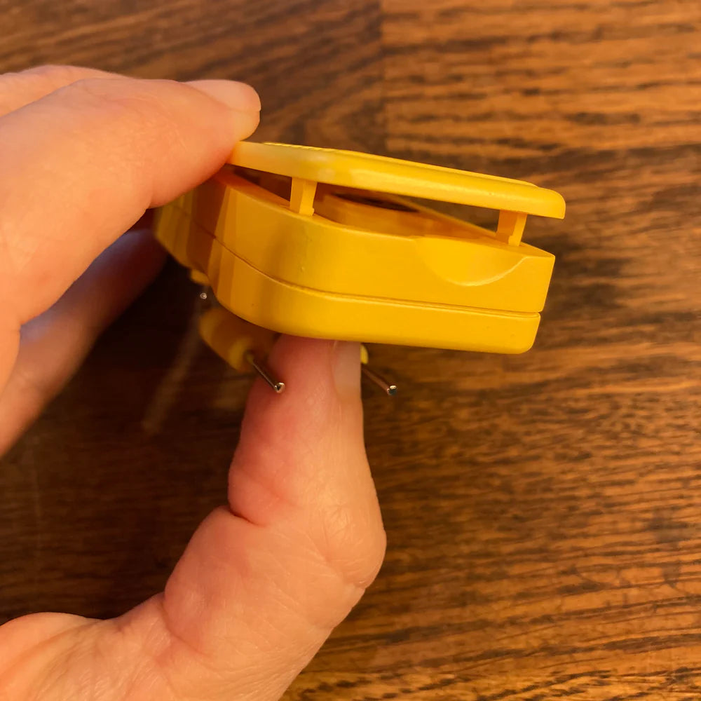 Hand closing the yellow plastic lid on the component against a wooden background