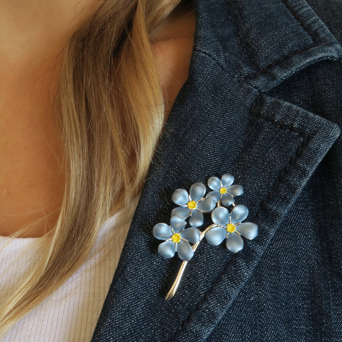 A ladies shoulder with a jacket zoomed into a silver plated forget-me-not brooch