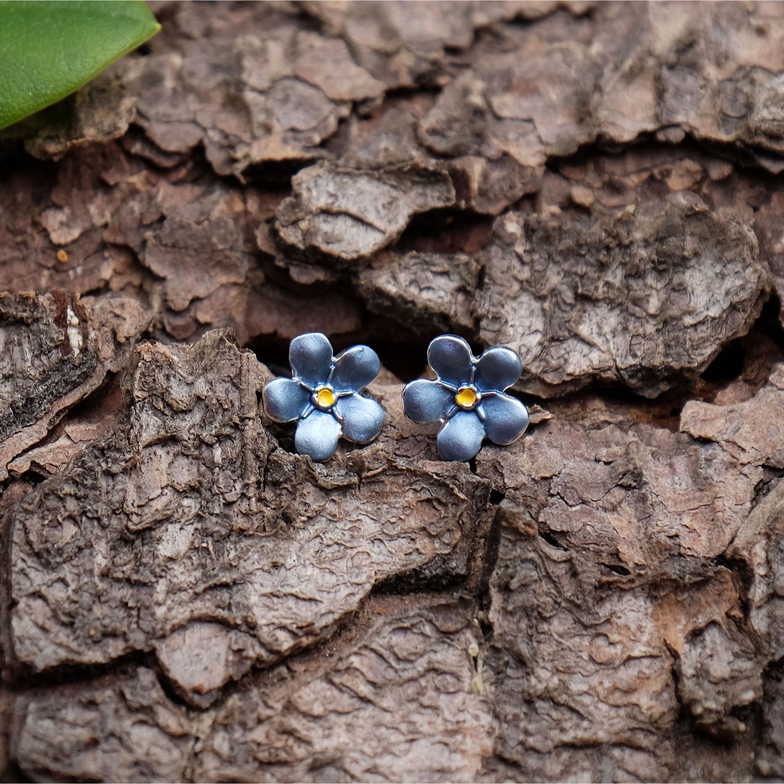 Mini forget-me-not stuff earrings on bark background with a green leaf