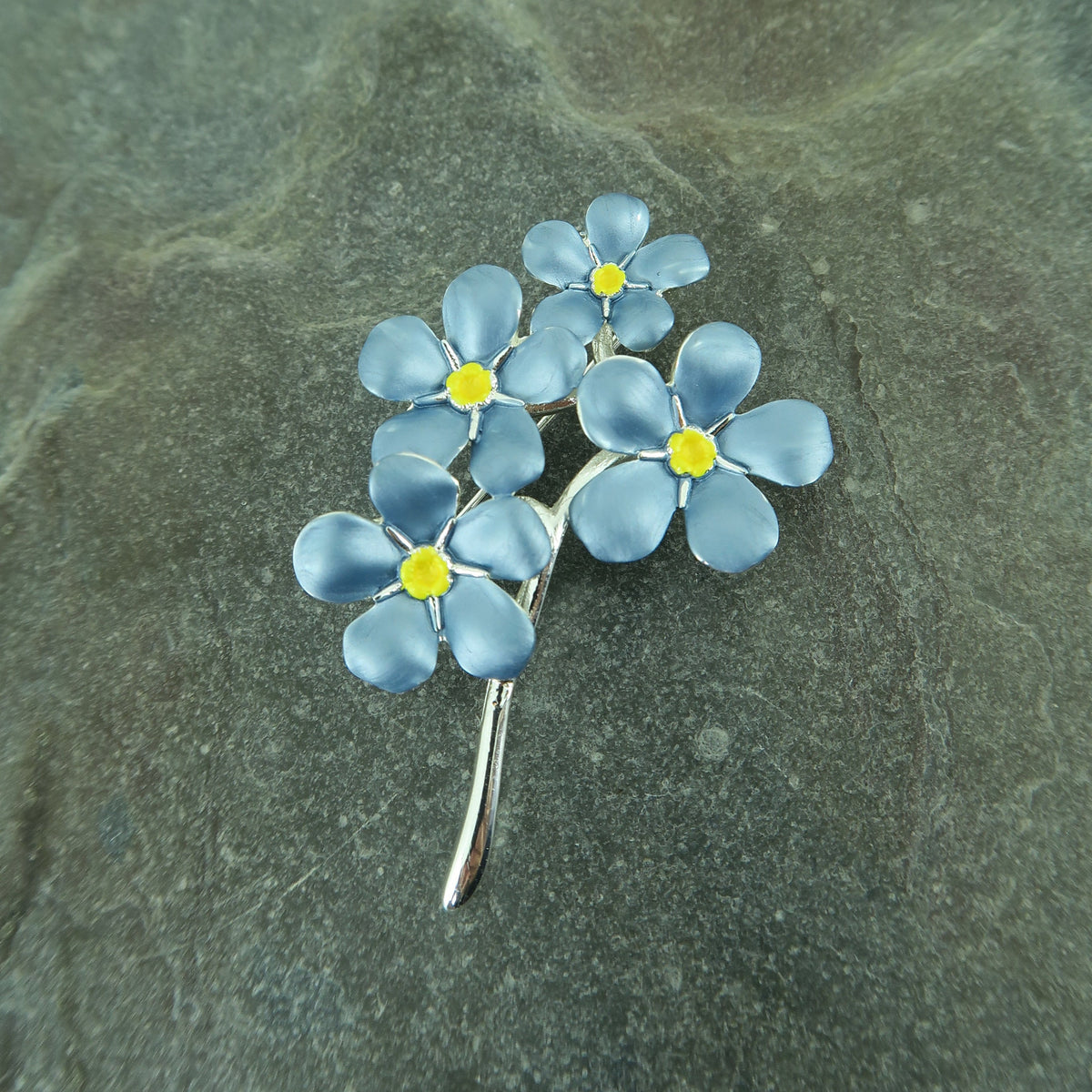 A blue silver-plated forget-me-not brooch on a stone background