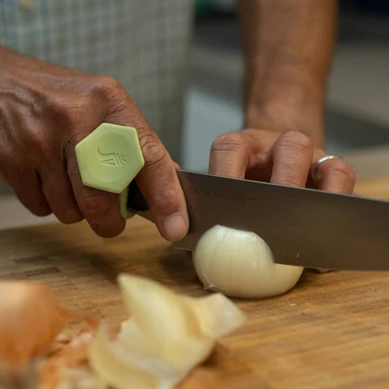 Person cutting an onion on a wooden cutting board with a knife with a toggle.