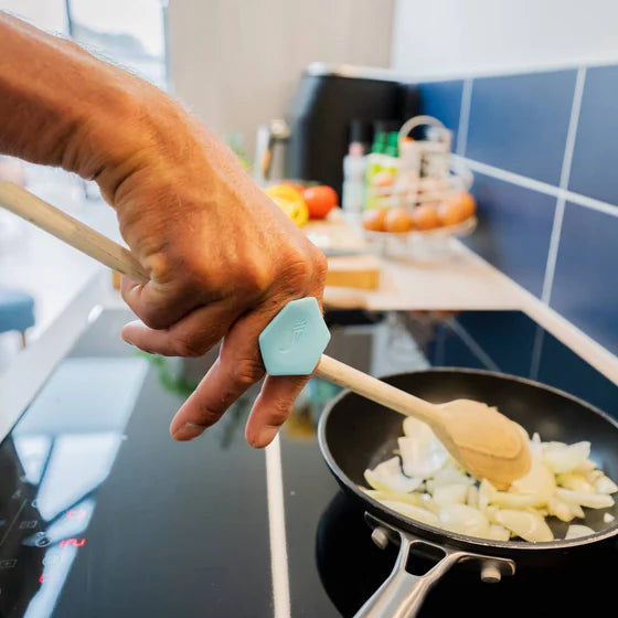 Person cooking onions in a pan with a wooden spoon held in a toggle on a stove.