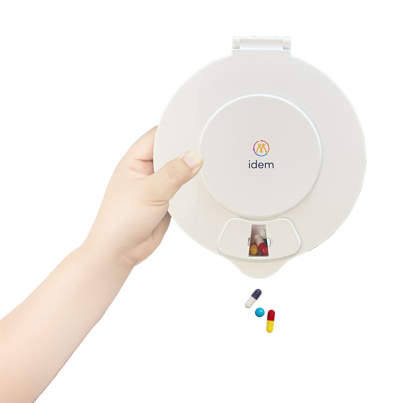 White idem pill dispenser held by a hand - allocated tablets are dispensed from a small window in the dispenser.