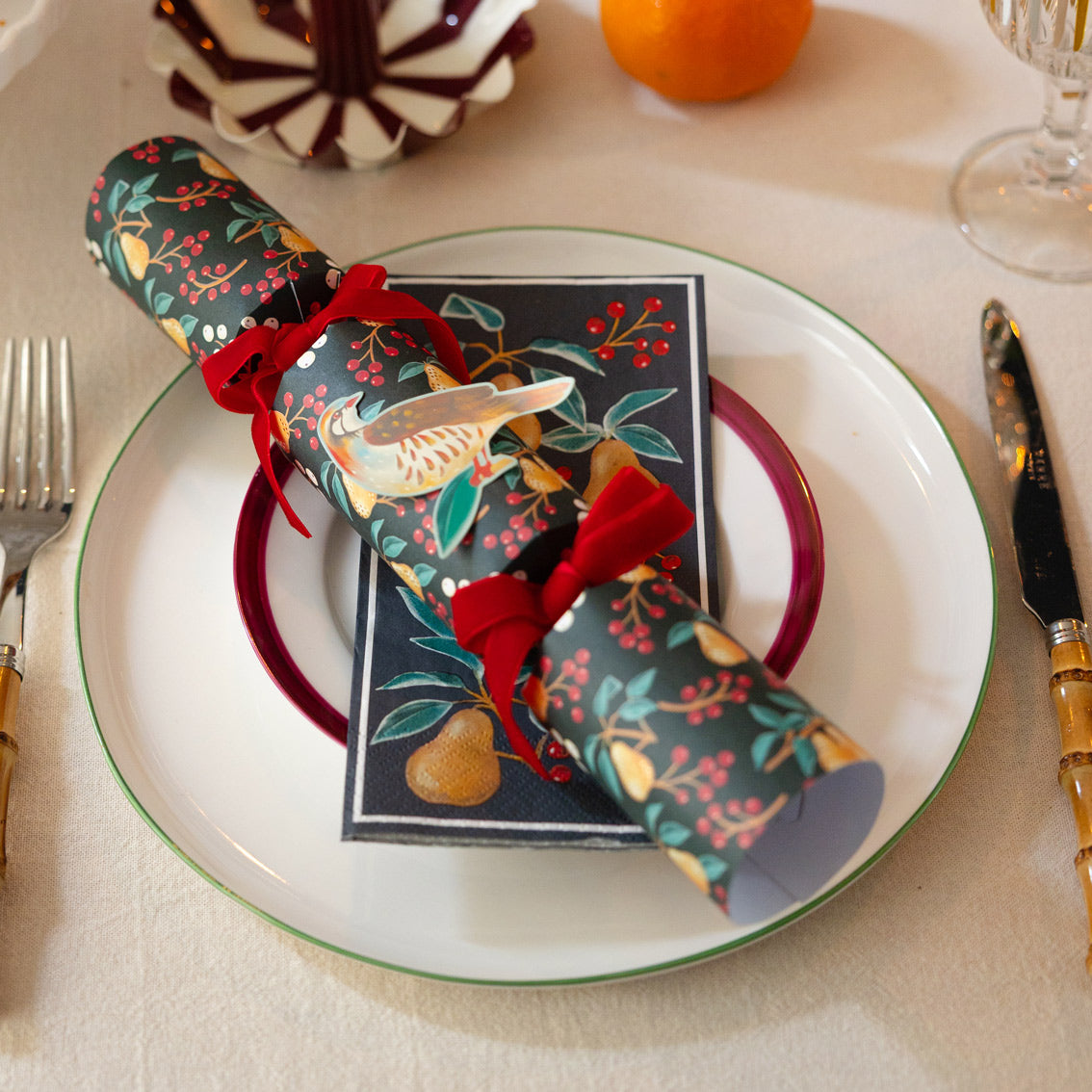 Decorative Christmas cracker with a napkin on a plate with cutlery and a glass.