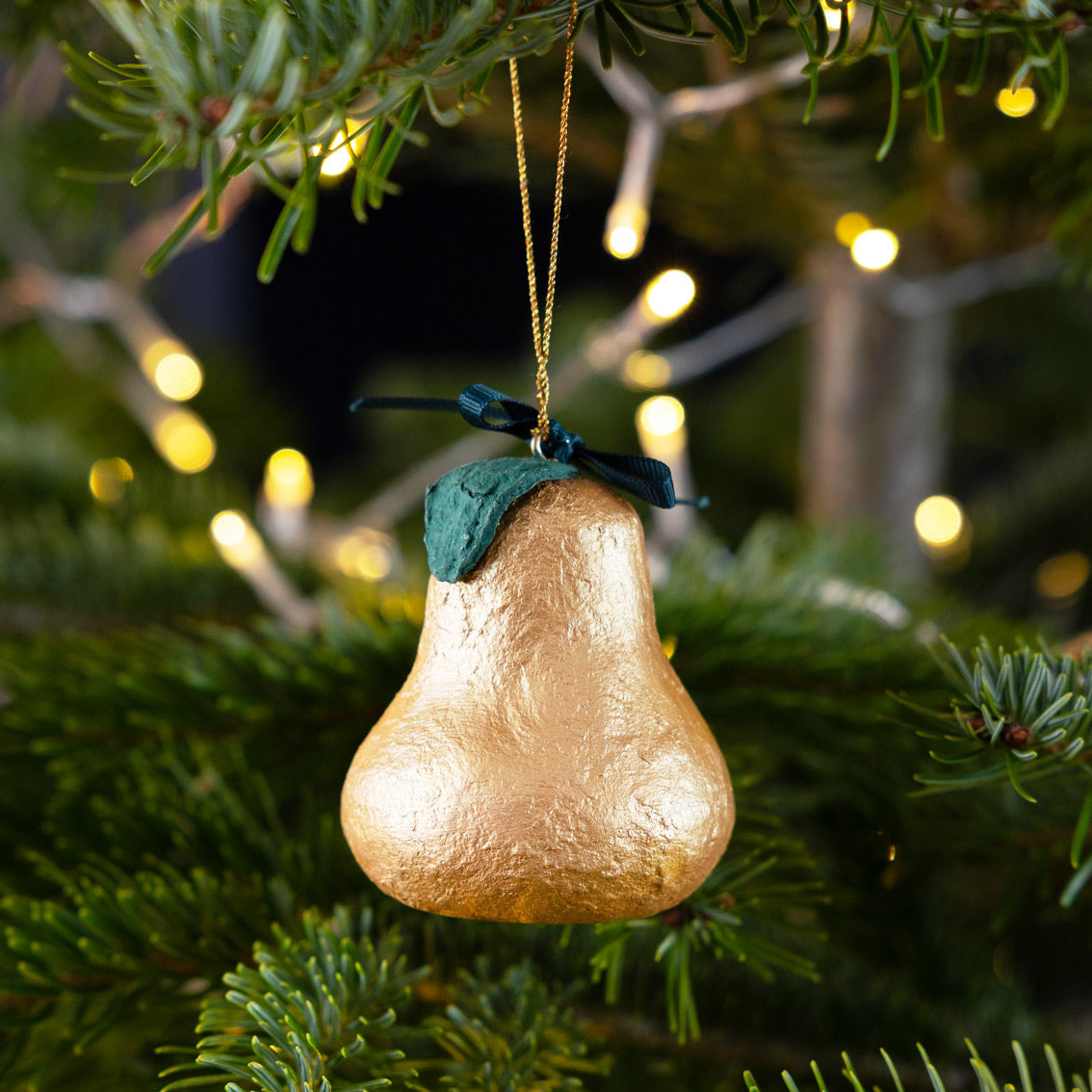 Gold pear-shaped ornament with a green leaf on a Christmas tree with blurred lights in the background