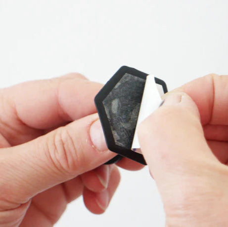 Close-up of hands holding a small black silicone grip, peeling off the sticky label against a light background