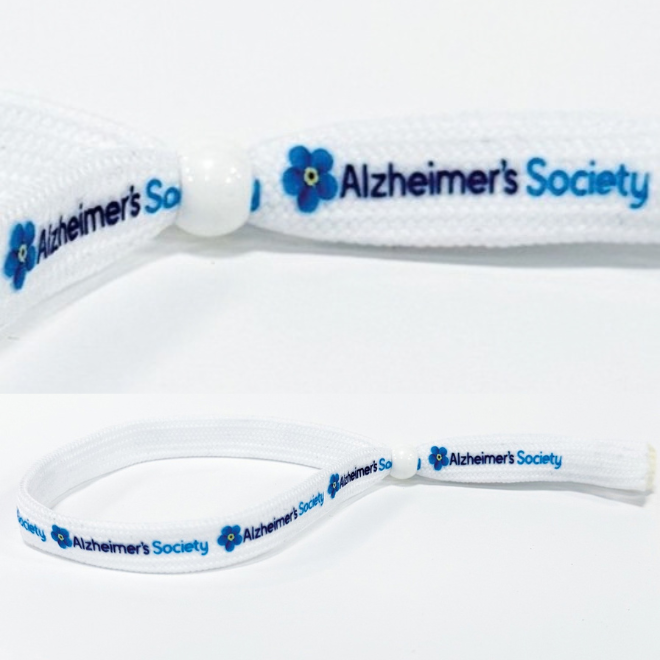 White flat shoelace style fabric wristband in a loop with a white plastic bead sliding closure. Alzheimer's Society logo including the forget-me-not flower is printed several times in full colour on the wristband.